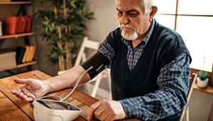 一位年长的成年男性坐在桌前用血压仪量血压